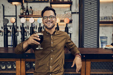 Portrait of a smiling man raising his beer glass in a pub - ZEDF03682