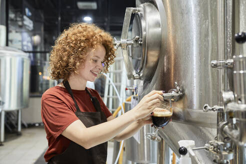 Frau arbeitet in einer Handwerksbrauerei und zapft Bier aus einem Tank - ZEDF03703