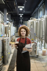 Porträt einer selbstbewussten Frau, die ein Klemmbrett und ein Bierglas in einer Handwerksbrauerei hält - ZEDF03710