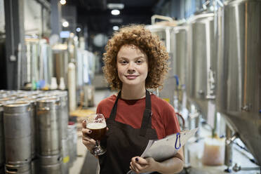 Porträt einer selbstbewussten Frau, die ein Klemmbrett und ein Bierglas in einer Handwerksbrauerei hält - ZEDF03711