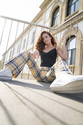 Surface level view of beautiful woman sitting on footbridge in city during sunny day - MTBF00614