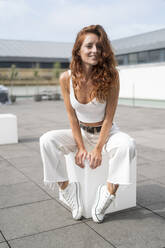 Beautiful redhead woman sitting on white cube - MTBF00629