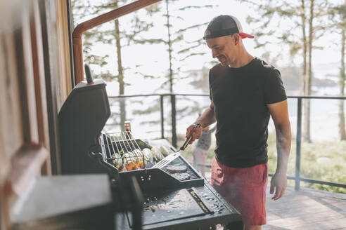 Mann kocht auf dem Grill, während er auf der Terrasse steht - CMSF00122