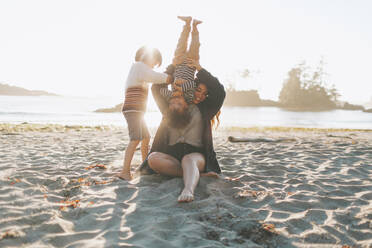 Mother playing with children while sitting on sand at beach - CMSF00123