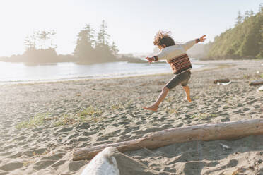 Junge mit ausgestreckten Armen springt am Strand - CMSF00124