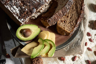 Draufsicht auf frisch geschnittenes Vollkornbrot mit Avocado und Käse für ein gesundes Nährstofffrühstück auf dem Küchentisch - ADSF12626