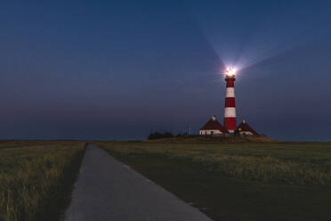 Germany, Schleswig-Holstein, Westerhever, Empty country road stretching past Westerheversand Lighthouse at dusk - KEBF01613