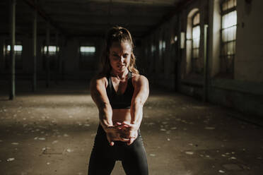 Athlete stretching arms while standing at abandoned factory - GMLF00522