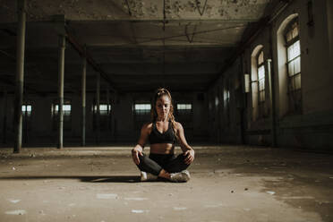 Athlete meditating while sitting at abandoned factory - GMLF00528