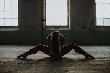 Woman practicing yoga while sitting on floor at abandoned factory - GMLF00537