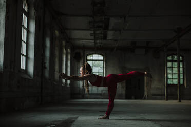 Woman practicing warrior 3 pose at abandoned factory - GMLF00540