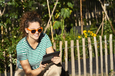 Junge Frau benutzt Tablet im Garten - FMKF06292