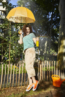 Young laughing woman with umbrella and limonade in garden - FMKF06294