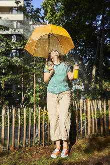 Young laughing woman with umbrella and limonade in garden - FMKF06295