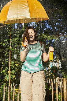 Young laughing woman with umbrella and limonade in garden - FMKF06296