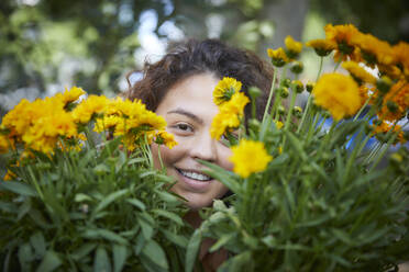 Portrait of smiling woman with yellow flowers in garden - FMKF06300