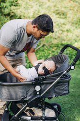 Young man putting baby boy in carriage at park - DCRF00723