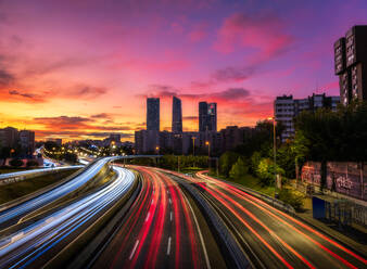 Drone view of cityscape with luminous highway in long exposure and skyscrapers under sunset sky - ADSF12681