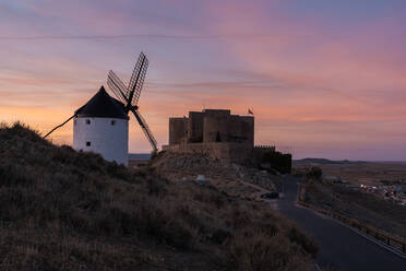 Aged windmill located on rocky cliff near medieval castle against cloudy sundown sky in countryside - ADSF12730