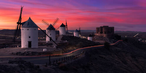 Aged windmills located on rocky cliff near medieval castle against cloudy sundown sky in countryside - ADSF12732