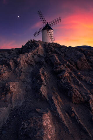 Aged windmill located on a rocky cliff against cloudy sundown sky in countryside stock photo
