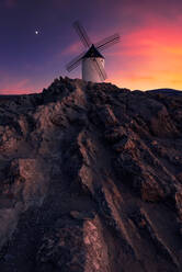 Gealterte Windmühle auf einer felsigen Klippe gegen bewölkten Sonnenuntergang Himmel auf dem Lande - ADSF12733