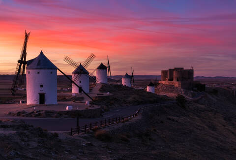 Aged windmills located on rocky cliff near medieval castle against cloudy sundown sky in countryside stock photo