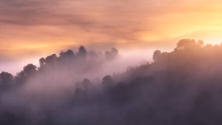 Rough Bergkette mit Bäumen gegen helle Sonnenaufgang Himmel in dunstigen Morgen in der Natur gelegen - ADSF12741