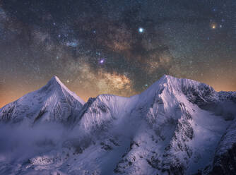 Amazing view of white snowy mountain range under incredible night starry sky with breaking rays of rising sun from behind mountains in winter evening - ADSF12742