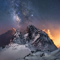 Amazing view of white snowy mountain range under incredible night starry sky with breaking rays of rising sun from behind mountains in winter evening - ADSF12746