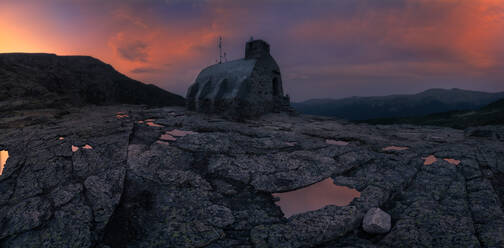 Picturesque landscapes of rocky cliffs with small stone house locating in middle of mountains against cloudy sky at sunset in beautiful evening - ADSF12748