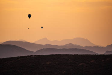 Silhouetten von fernen Heißluftballons fliegen gegen den Sonnenuntergang Himmel über hügeligem Gelände - ADSF12765