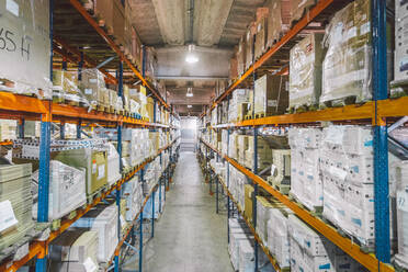 From above of empty narrow passage between big metal shelves with different packages and boxes in warehouse - ADSF12783