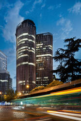 Long exposure of city traffic along street with glass exteriors of skyscrapers and blue sky in downtown at twilight in Spain - ADSF12833