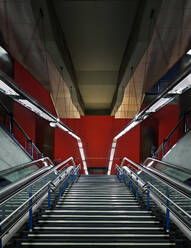 Breite graue Treppe mit leeren Rolltreppen, die zum Ausgang einer modernen geräumigen U-Bahn-Station mit roten Wänden und aufgehängten Lampen in Spanien führt - ADSF12842