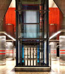 Komfortabler transparenter Aufzug in der Mitte des Flurs einer modernen Metrostation mit bunten Wänden und glänzenden Metallsäulen in Madrid - ADSF12844