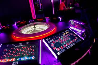 Casinotisch mit modernem Roulette und digitalen Bildschirmen, beleuchtet von Neonröhren im dunklen Casino - ADSF12869