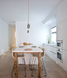 Interior of contemporary kitchen in Scandinavian style with dining table and bar stools - ADSF12885