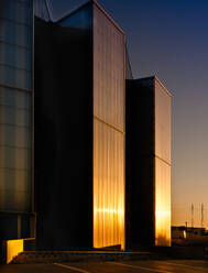 Außenansicht eines modernen Glasgebäudes, in dem sich die untergehende Sonne gegen den wolkenlosen Himmel spiegelt, abends auf einer Stadtstraße - ADSF12894