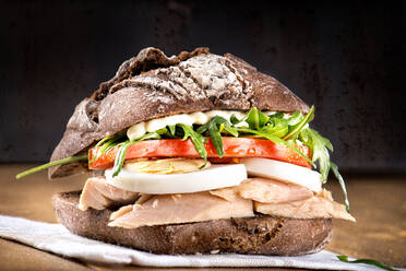 Nahaufnahme von leckeren rustikalen Brot Sandwich mit Tomaten, Salat, Thunfisch hart gekochtes Ei und Mayonnaise auf Holzbrett auf schwarzem Hintergrund serviert - ADSF12911