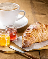 Delicious freshly baked croissant served with fruit marmalade and cup of hot coffee with milk on wooden table - ADSF12925