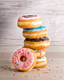 Stapel von leckeren süßen sortierten Donuts mit bunten Zuckerguss und Streuseln auf hölzernen Hintergrund platziert - ADSF12926