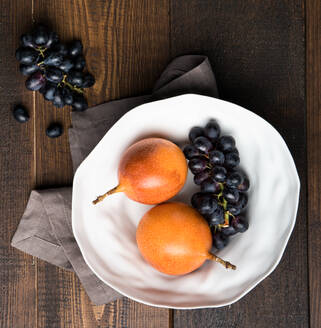 Top view of ripe passion fruits and bunches of purple grapes placed on wooden table in kitchen - ADSF12932