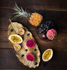 Top view of tasty passion fruits and pitaya on dish arranged with pineapple and purple grapes on wooden table - ADSF12938