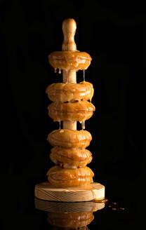 Köstliche Turm von gebratenen Krapfen auf hölzernen Halter alle mit glänzenden goldenen Honig gegen schwarzen Hintergrund bedeckt platziert - ADSF12950
