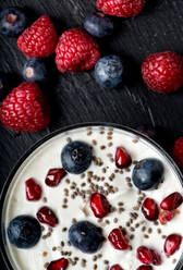 Top view of round bowl with fresh dairy yogurt topped with pomegranate seeds and blueberry with raspberry - ADSF12951