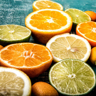 Hoher Winkel von geschnittenen frischen saftigen süßen Orangen in Komposition mit reifen sauren Zitronen und Limetten auf türkisfarbener Oberfläche - ADSF12965