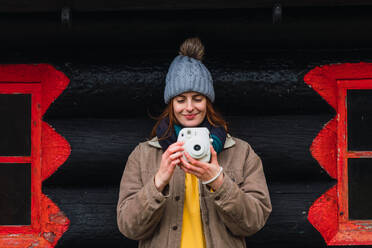 Frau in Winterkleidung vor einer Holzhütte beim Fotografieren - ADSF12972