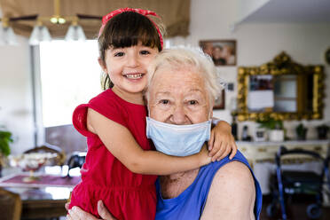 Grandmother and little girl spending family time together at home, with face mask - GEMF04096