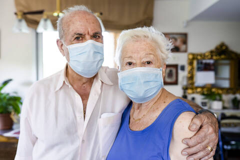 Älteres Ehepaar trägt Schutzmasken zu Hause, lizenzfreies Stockfoto